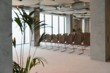 Geniş oditoryum salonu boş sandalyeler, büyük pencereler ve kurumsal etkinlik, toplantı ya da seminer için bir projektör sunuyor.