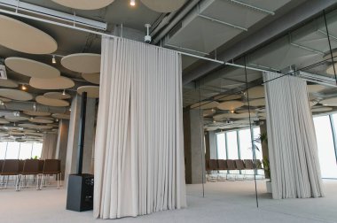 Bej perdelerin, aynalı bir duvarın ve boş sandalyelerin yer aldığı geniş bir iç dizayn, bir etkinliğe ya da toplantıya hazır.