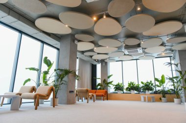 Şık mobilyaları, sayısız kapalı bitkileri ve yuvarlak akustik panelleri olan bir tavanı olan modern ofis salonu.