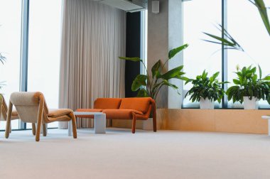 Konforlu sandalyeler, bir kanepe ve yeşil bitkilerin yer aldığı çağdaş çalışma alanı, misafirperver ve modern bir rahatlama ortamı yaratıyor.