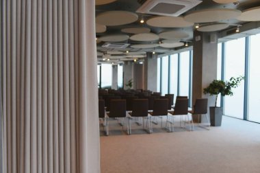 Sıralar dolusu sandalye, büyük pencereler ve bir etkinlik için hazırlanmış akustik tavan panelleriyle modern konferans salonu.