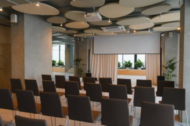 Boş bir konferans odası, sıra sıra sandalyeler, boş bir projeksiyon ekranı, ve bir projektör, şirket etkinlikleri için hazır.