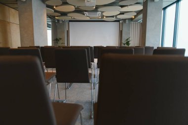 Seminer ya da iş toplantısı için hazırlanmış, boş projektör ekranlı sıra sıra sandalyelerle konferans odası