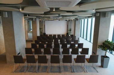 Boş projektör ekranına bakan sandalyelerle dolu çağdaş seminer salonu, sunumlar ve kurumsal etkinlikler için ideal