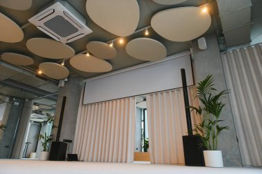 Geri çekilebilir projeksiyon ekranı olan konferans odası, ses dağıtıcı tavan panelleri ve modern ses ekipmanları
