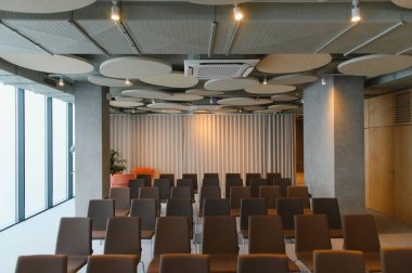 Modern konferans odası içi boş sandalyeler, akustik tavan tasarımı, ve büyük pencereli, kurumsal toplantı için hazır.