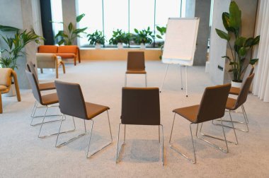 Kahverengi sandalyeler beyaz tahtaya dönük bir daire oluşturarak katılımcıların ortak bir atölye ya da terapi çemberi kurmalarını bekliyor.