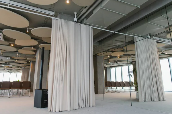 Bej perdelerin, aynalı bir duvarın ve boş sandalyelerin yer aldığı geniş bir iç dizayn, bir etkinliğe ya da toplantıya hazır.