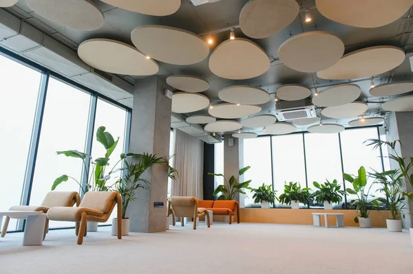 Şık mobilyaları, sayısız kapalı bitkileri ve yuvarlak akustik panelleri olan bir tavanı olan modern ofis salonu.