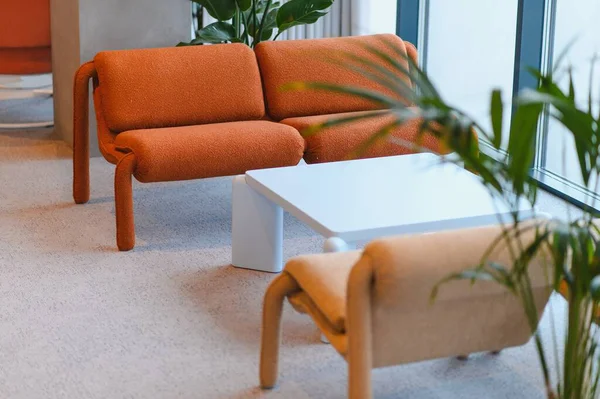 Portakal rengi bir modüler kanepe, beyaz bir kahve masası ve çağdaş bir bekleme alanı yaratan minimalist tasarım elementleri içeren modern bir iç mekan.