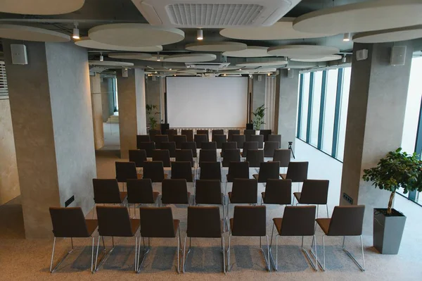 Boş projektör ekranına bakan sandalyelerle dolu çağdaş seminer salonu, sunumlar ve kurumsal etkinlikler için ideal