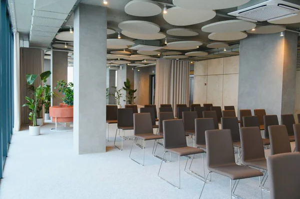 Boş sandalyeler, minimalist tasarım, beton duvarlar, yemyeşil bitkiler ve akustik tavan panelleri ile konferans salonu etkinlik düzenleme