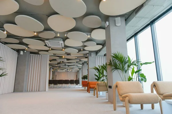 Modern tasarımın sergilendiği ofis salonu, minimalist mobilyalar, bitkiler, akustik tavan panelleri ve büyük cam pencereler