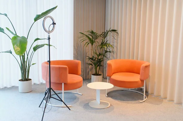 Çağdaş stüdyo alanı iki turuncu koltuk, bir beyaz kahve masası ve bir ışıklandırma düzeneği içeriyor.