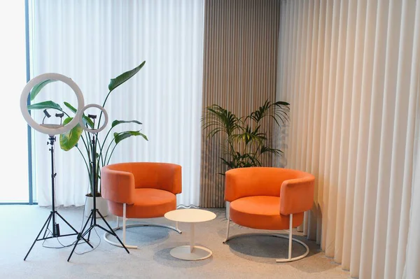 İki turuncu koltuk, bir beyaz kahve masası ve içerik yaratmak için profesyonel halka ışıkları içeren modern stüdyo alanı