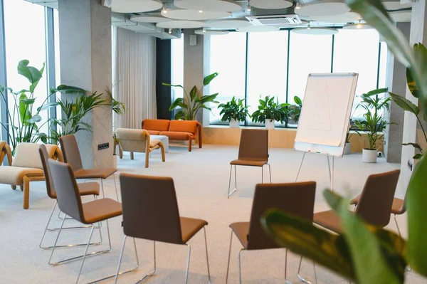 Konferans odasında daire şeklinde sıralanmış sandalyeler, ters çizelge ve yeşil kapalı alan bitkileri rahat bir ortam yaratıyor.