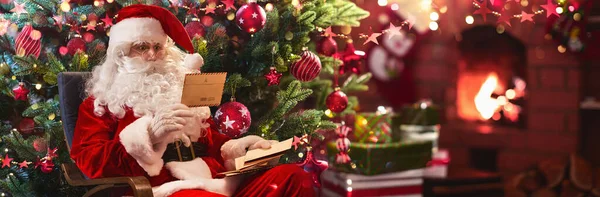 Papai Noel sentado em seu quarto e lendo lista de desejos de Natal — Fotografia de Stock