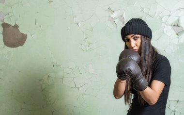 Genç kız boksör yeşil çatlamış bir duvarın arkasında koruyucu bir duruş sergiliyor.