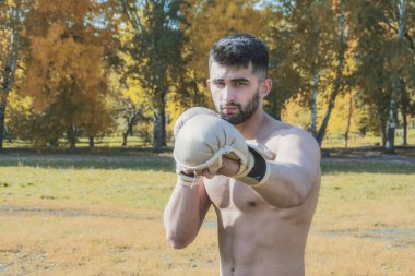 Dövüş eldivenleri giymiş genç bir dövüş sanatları dövüşçüsü bir elle saldırıyor ve kameraya bakıyor.