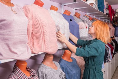 Genç alışveriş yapan kız mağazada kadın giysilerini inceleyip dokunuyor.