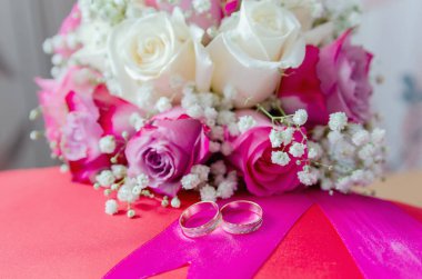 Düğün çiçeği beyaz ve kırmızı güller ve iki alyans kırmızı bir yastıkta yatıyor. 