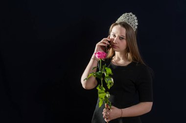 Kafasında diyabet olan bir prenses suretindeki genç kız karanlık bir arkaplanda duruyor ve telefonda konuşuyor. Kameraya bak.