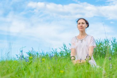 Güzel genç bir kadın yeşil bir çimenlikte oturuyor ve meditasyon yapıyor. Açık hava aktiviteleri.