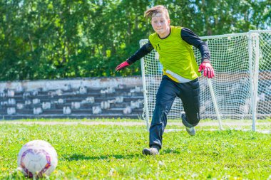 Genç bir futbolcu çimlerin üzerinde uçan topu yakalamak için sahada koşuyor. Genç futbolcuların eğitimi.