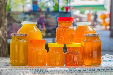 Masanın üzerinde cam kavanozlar ve bal dolu plastik kaplar var ve bal fuarında satılmaya hazır..