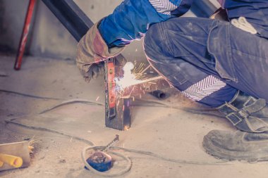 Kaynak makinesinin yardımıyla çalışan erkek kaynakçı, gelecekteki merdivenlerin metal yapısını bir konut binasında birleştiriyor. Sıcak metal kıvılcımları uçuşuyor.