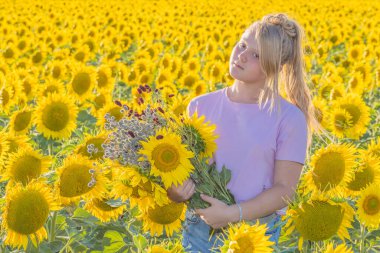 Parlak güneşli bir gün. Büyük bir buket ayçiçeği ve kır çiçeğiyle genç bir kız sarı bir tarlanın ortasında duruyor. Kameraya bakıyor. Açık hava eğlencesi.