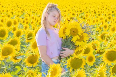 Parlak güneşli bir gün. Büyük bir buket ayçiçeği ve kır çiçeğiyle genç bir kız sarı tarlanın ortasında gözleri kapalı duruyor. Açık hava eğlencesi.