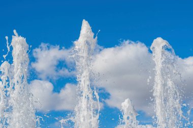 Mavi bulutlu yaz gökyüzünün arka planına su akıntısı ve sıçramaları. Çeşme.