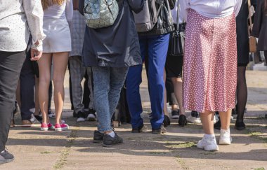 Bir grup genç, sırtı kameraya dönük bir şekilde bir şehir caddesinde dikiliyor..