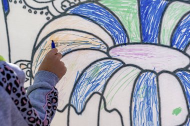 Mavi keçeli kalemle çocuk eli beyaz bir tuvale çizilmiş çiçek yapraklarını boyar. Sokak çizimi.