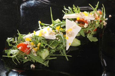 Arugula ve peynir siyah tabakta, yağlı.