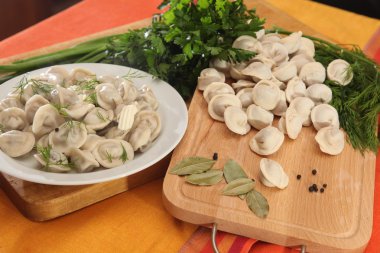 Tahta kesme tahtasının üzerinde pişmemiş mantı ve yeşillik.