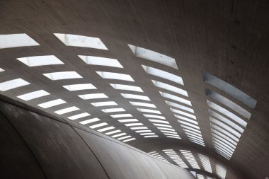 Beton koridorda güneş ışığı altında bir sürü pencere var.