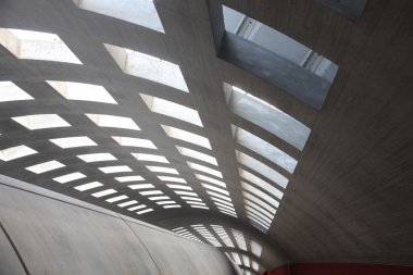 Beton koridorda güneş ışığı altında bir sürü pencere var.