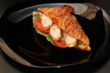 Tavuklu sandviç ve siyah tabakta sebze.