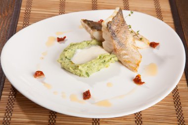 Beyaz tabakta patates püresi ve peynir sosu ile turna balığı.