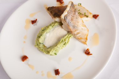 Beyaz tabakta patates püresi ve peynir sosu ile turna balığı.