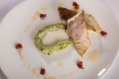 Beyaz tabakta patates püresi ve peynir sosu ile turna balığı.