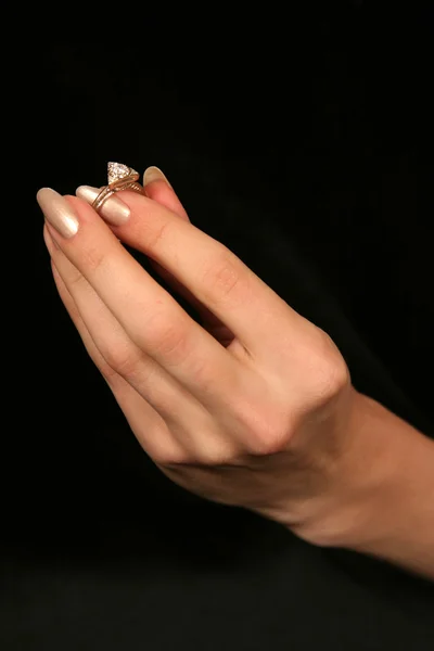 female hand holding fingers diamond ring on black background