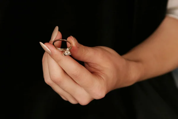 female hand holding fingers diamond ring on black background