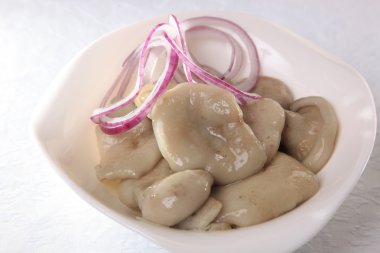 Beyaz tabakta soğanlı tuzlanmış mantar.