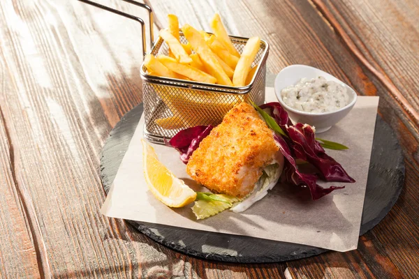 fish with fries and tartar sauce on wooden table