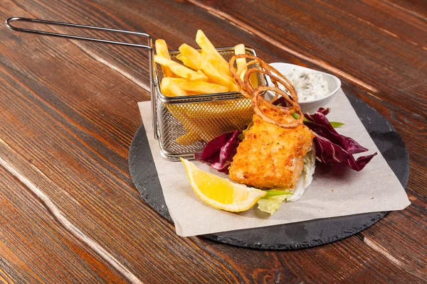fish with fries and tartar sauce on wooden table