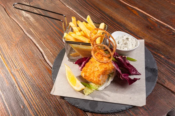 fish with fries and tartar sauce on wooden table