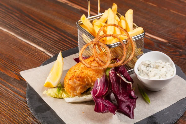 fish with fries and tartar sauce on wooden table